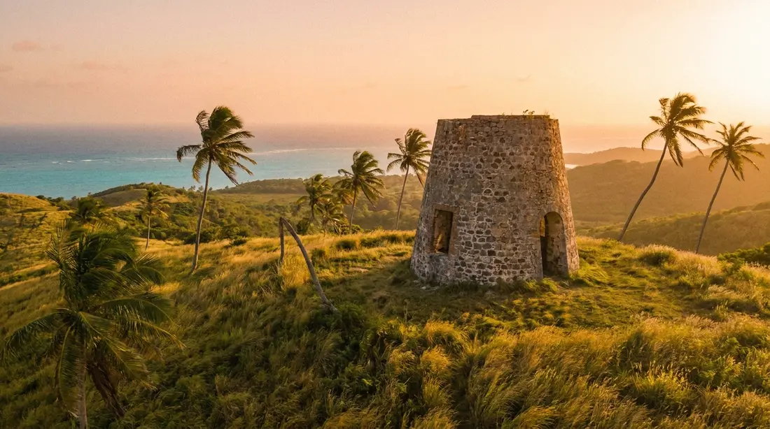 A Danish-era stone sugar-mill windmill ruin on a green hillside above the sea at golden hour
